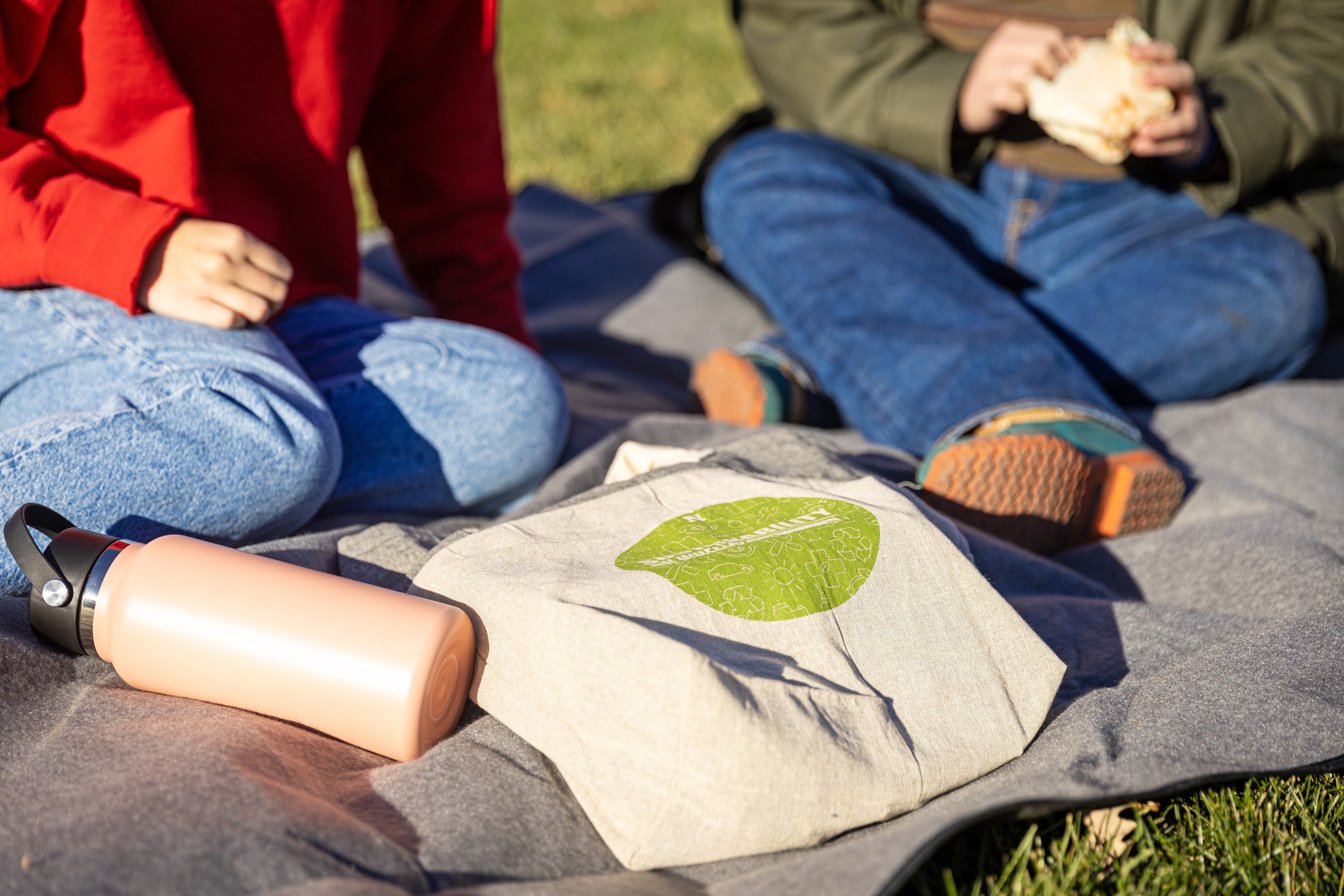 Two students sit outside on a picnic blanket and talk to each other.