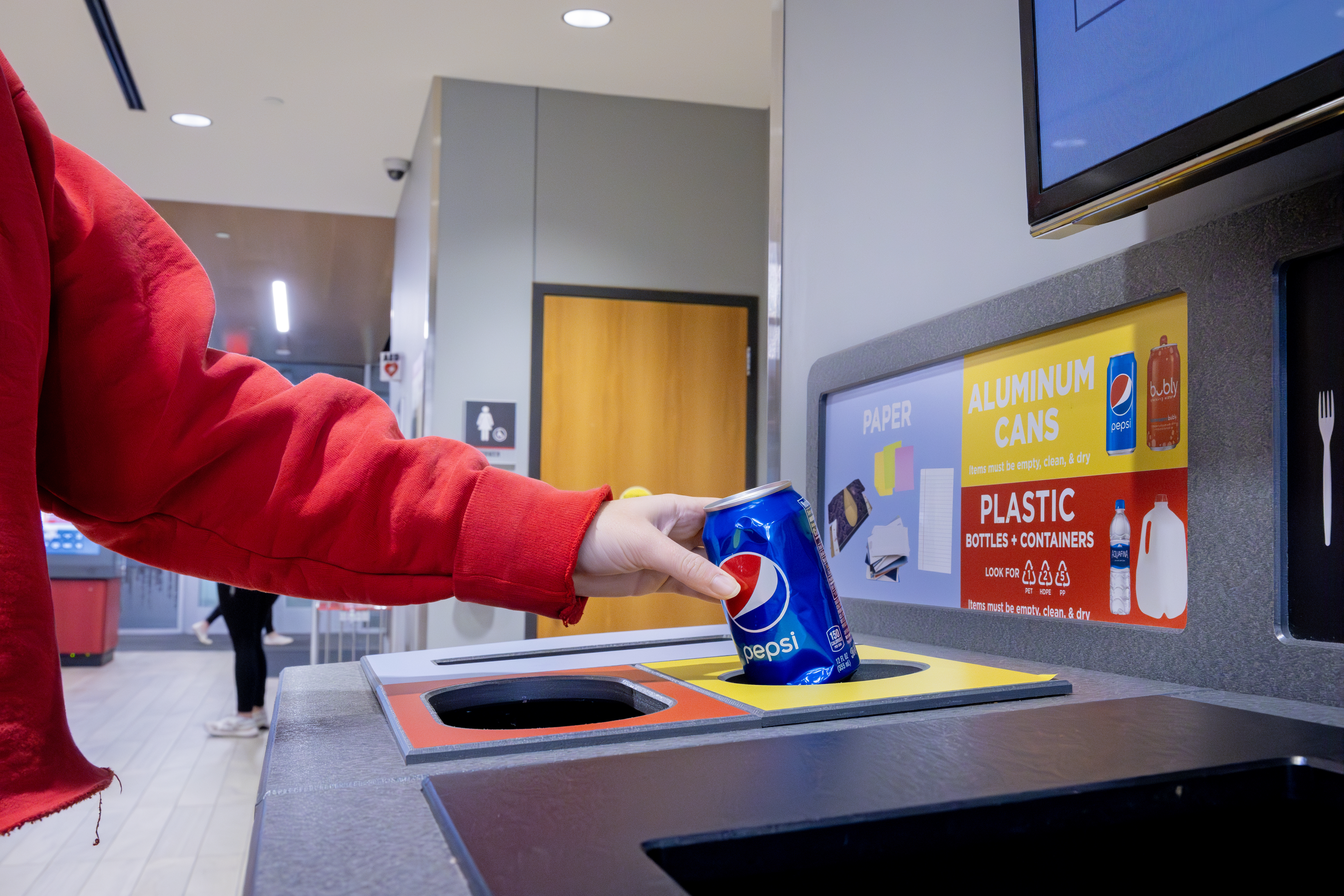 A student recycles a Pepsi can in the correct slot for aluminum cans in an All in the Hall recycling station