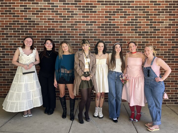 Seven people in sustainable fashion outfits standing against a brick wall outdoors.