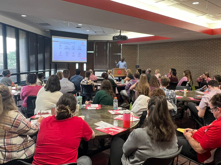 New employees sit at circular tables facing a speaker at the UNL new employee orientation